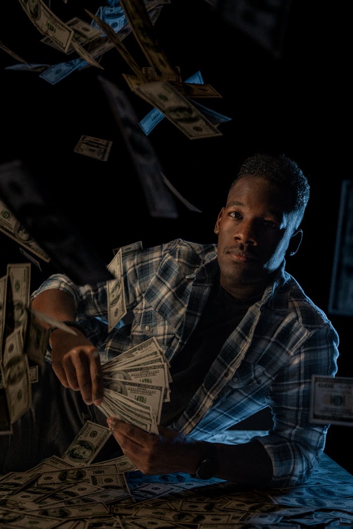 Man in a plaid shirt holding cash, surrounded by floating money in a studio setting.